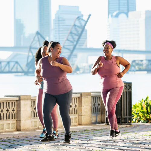 Three women jogging on a waterfront promenade, both in workout gear.