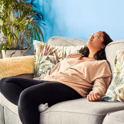 Woman resting with eyes open on a couch, serene indoor setting.