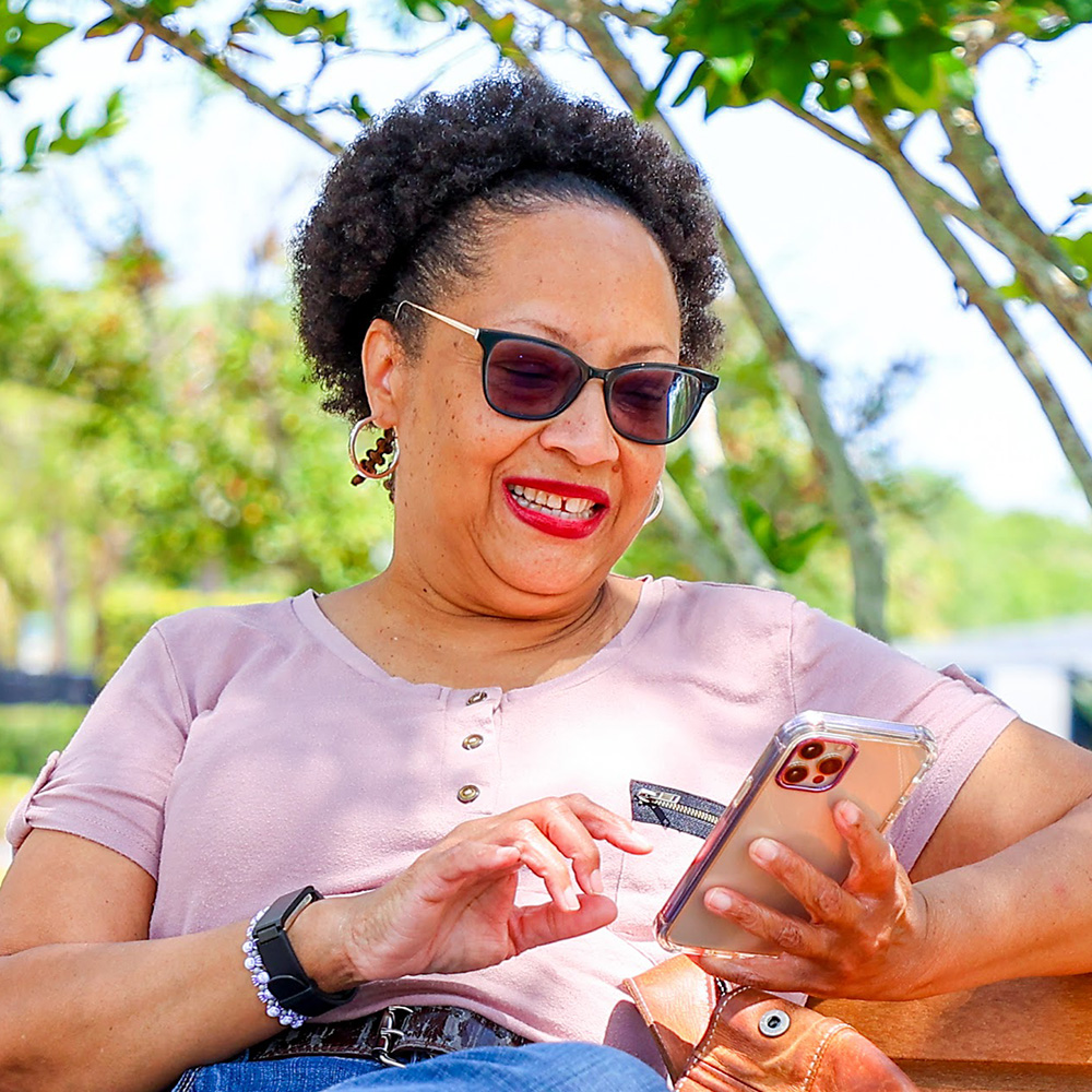 Cheryl, a stroke survivor and Kandu program graduate, sitting on a park bench using her phone.