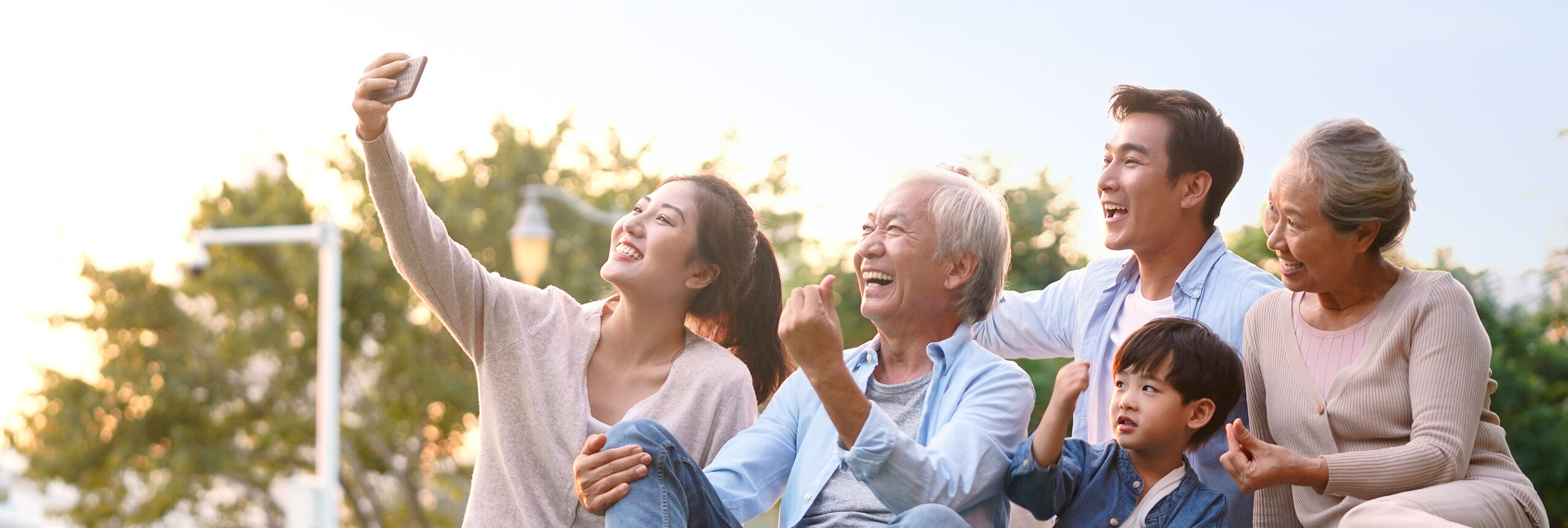 A multi-generational family smiling and taking a selfie in an outdoor setting.