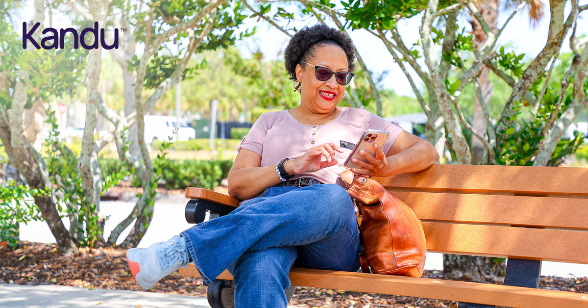 Cheryl, a stroke survivor and Kandu program graduate, sitting on a park bench using her phone.